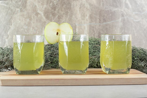 Trois verres de jus avec tranche de pomme sur planche de bois