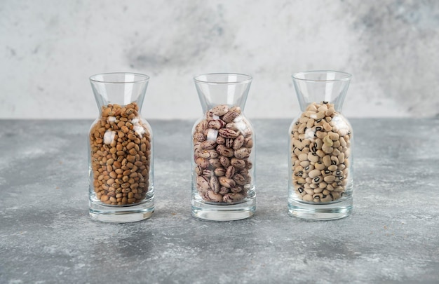 Trois verres de pot avec des haricots non préparés sur une table grise.