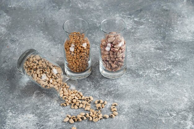 Trois verres de pot avec des haricots non préparés sur une table grise.