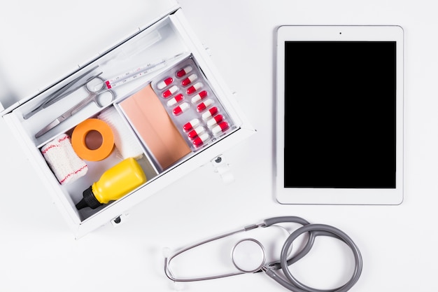 Trousse de premiers soins avec tablette numérique et stéthoscope sur fond blanc