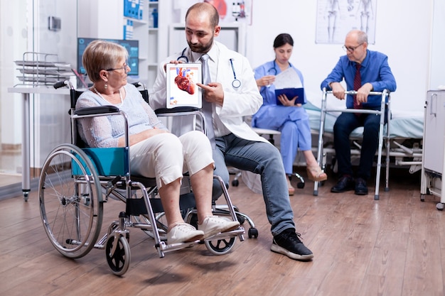 Photo gratuite trucs médicaux présentant un livret d'arythmies à une femme âgée handicapée assise en fauteuil roulant