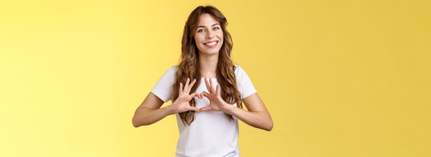 Photo gratuite tu es ma valentine tendre confiante fille adulte coiffure bouclée montre le geste du cœur près de la poitrine expresse