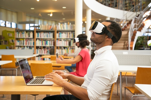 Étudiant adulte avec simulateur de réalité virtuelle dans une bibliothèque