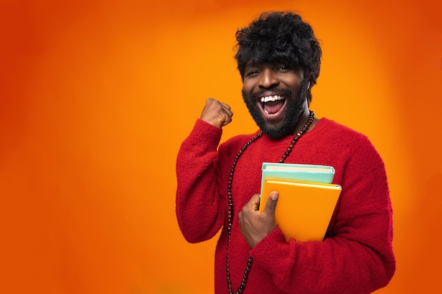 Étudiant afro-américain réussi tenant des livres sur fond orange