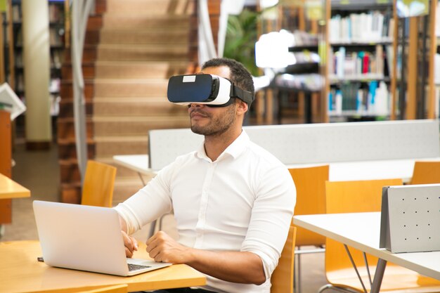Étudiant à l'aide d'un casque de réalité virtuelle pendant le travail en bibliothèque