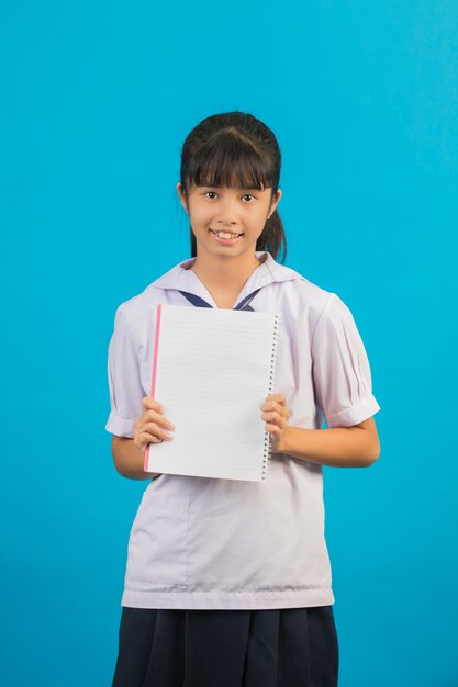 Étudiant asiatique avec fille cheveux longs tenant un cahier sur un bleu.