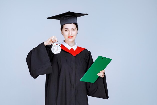 Étudiant diplômé avec diplôme tenant un réveil pour afficher l'heure. photo de haute qualité