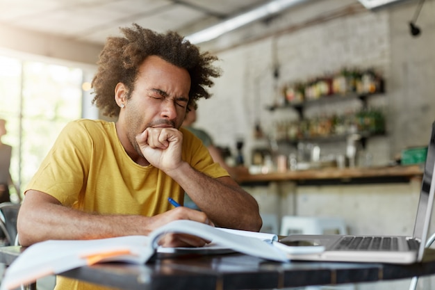 Étudiant diplômé européen noir endormi épuisé bâillant, couvrant la bouche avec le poing fatigué