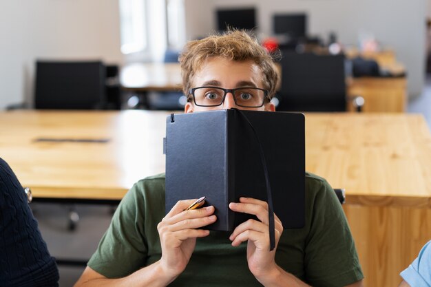 Étudiant effrayé se cachant derrière un cahier