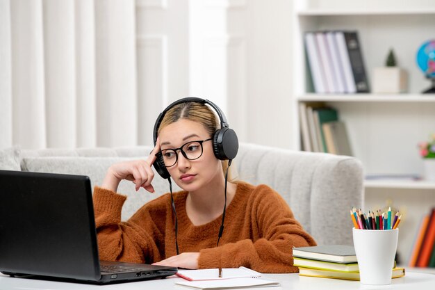 Étudiant en ligne jeune fille mignonne dans des verres et un pull orange étudiant sur la pensée informatique