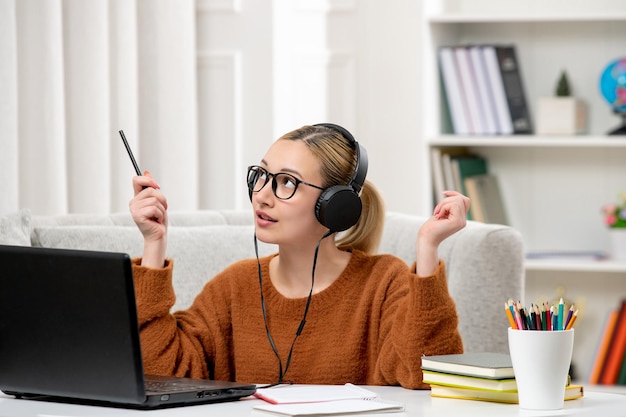 Étudiant en ligne jolie fille à lunettes et chandail étudiant sur ordinateur en levant la pensée