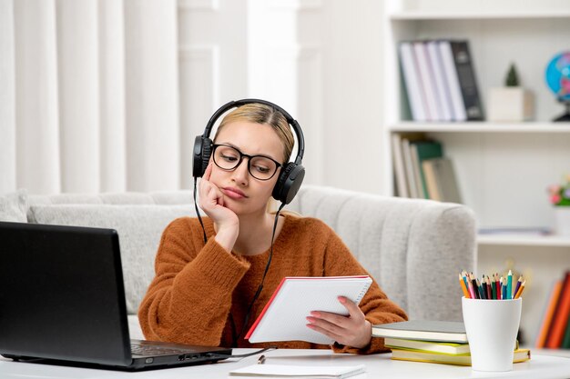 Étudiant en ligne jolie fille à lunettes et pull étudiant sur ordinateur pensant lire des notes