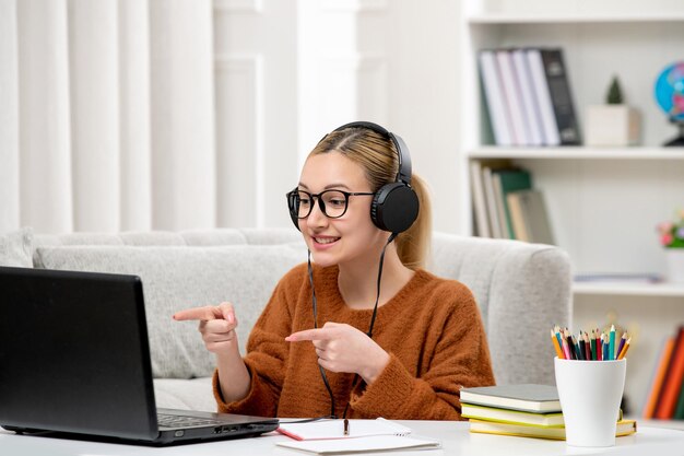 Étudiant en ligne jolie fille à lunettes et pull étudiant sur ordinateur souriant