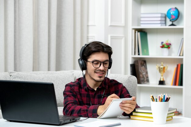 Étudiant en ligne mec mignon en chemise à carreaux avec des lunettes étudiant sur des notes d'écriture d'ordinateur