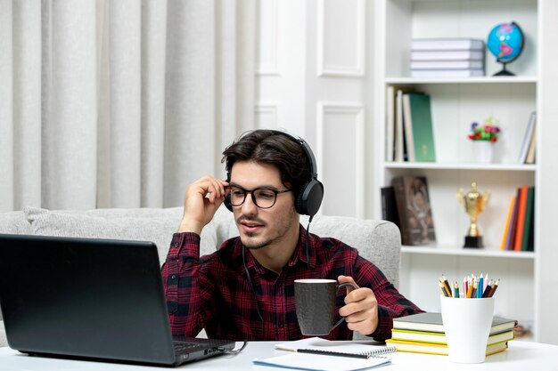 Étudiant en ligne mec mignon en chemise à carreaux avec des lunettes étudiant sur ordinateur en écoutant un conférencier