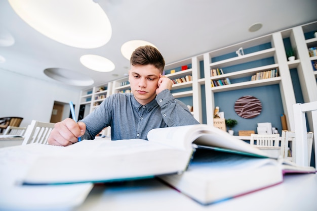 Étudiant en lisant avec des livres sur la table dans la bibliothèque