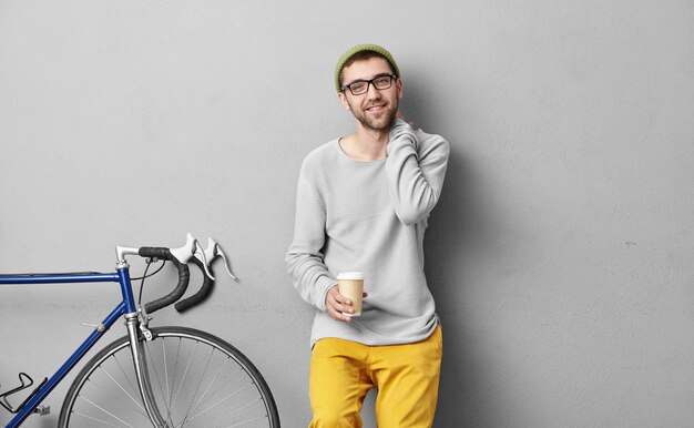 Étudiant à la mode rentrant chez lui à vélo après les cours, s'arrêtant, buvant du café à emporter, souriant agréablement tout en rencontrant son vieil ami, ayant une conversation agréable