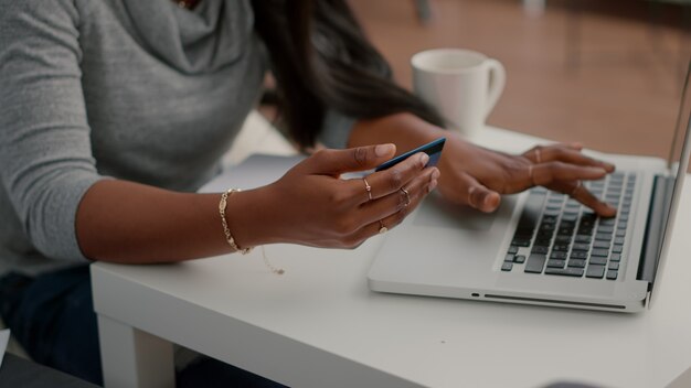 Étudiant noir tenant une carte de crédit dans les mains faisant des transactions électroniques à la recherche d'une boutique en ligne