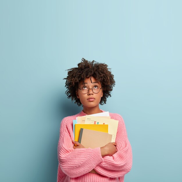 Étudiant travaillant dur concentré, porte des papiers, des manuels et un bloc-notes