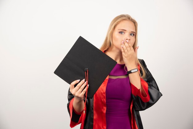 Étudiante blonde couvrant sa bouche sur blanc.