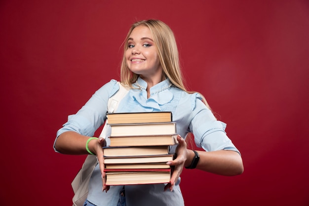 Étudiante blonde tenant une pile de livres et semble positive.