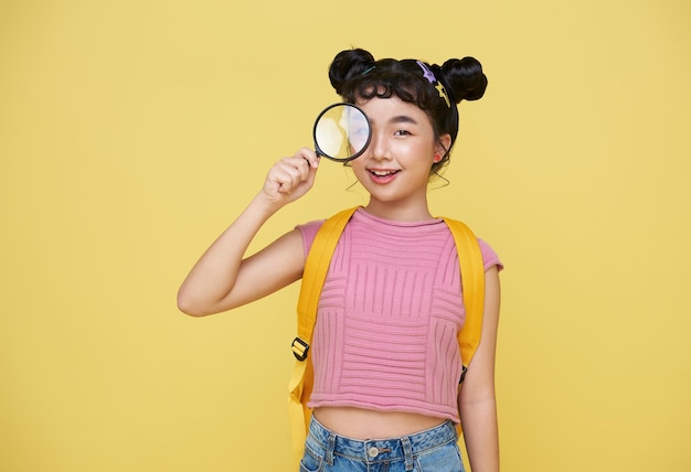 Étudiante enfant asiatique tenant une loupe et regardant la caméra avec une expression curieuse