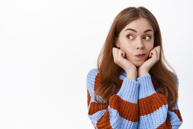 Étudiante mignonne pensant et regardant le texte promotionnel, s'appuyant sur les mains et regardant le logo du coin supérieur gauche avec un visage pensif, mur blanc