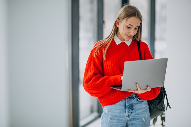 Étudiante avec ordinateur portable debout près de la fenêtre dans le couloir