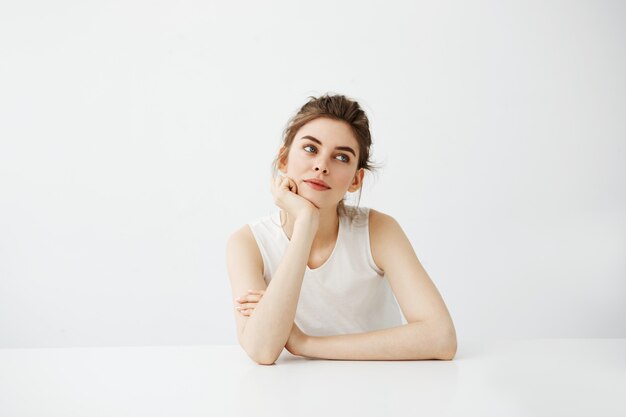 Étudiante rêveuse jeune belle femme assise à table rêvant de réfléchir sur fond blanc.