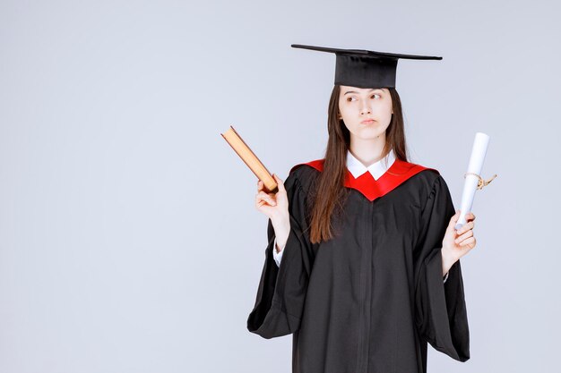 Étudiante en robe académique tenant un livre et un diplôme. photo de haute qualité