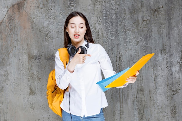 Étudiante avec sac à dos jaune et casque pointant vers le livre. Photo de haute qualité