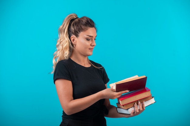 Étudiante tenant un gros stock de livres et ouvrant l'un d'entre eux.