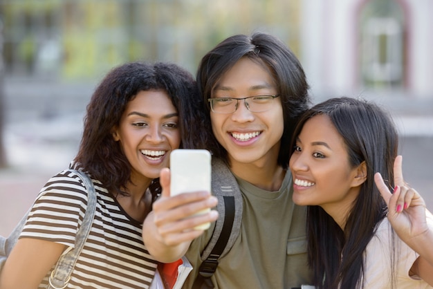 Étudiants heureux debout et faire du selfie à l'extérieur