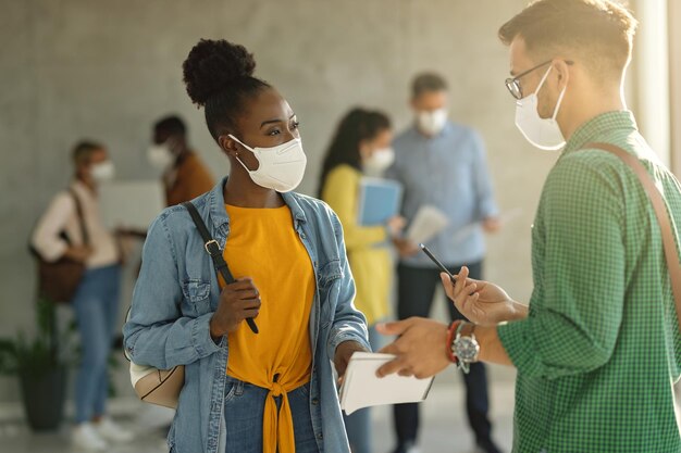 Étudiants universitaires avec des masques protecteurs parlant dans un couloir