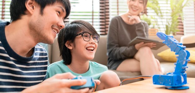 Étudier à la maison enfant garçon conceptasian avec père et mère bras de robot de contrôle réussi sur tablette numérique et clavier d'ordinateur famille heureuse recevant une leçon de robotique de contrôle de codage à la maison