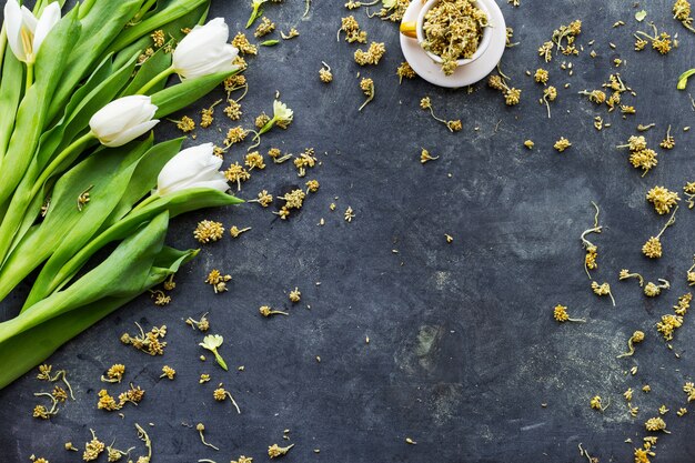 tulipes blanches avec des fleurs séchées dans une tasse sur une surface noire