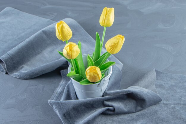 Tulipes jaunes dans un seau sur morceau de tissu, sur fond blanc.