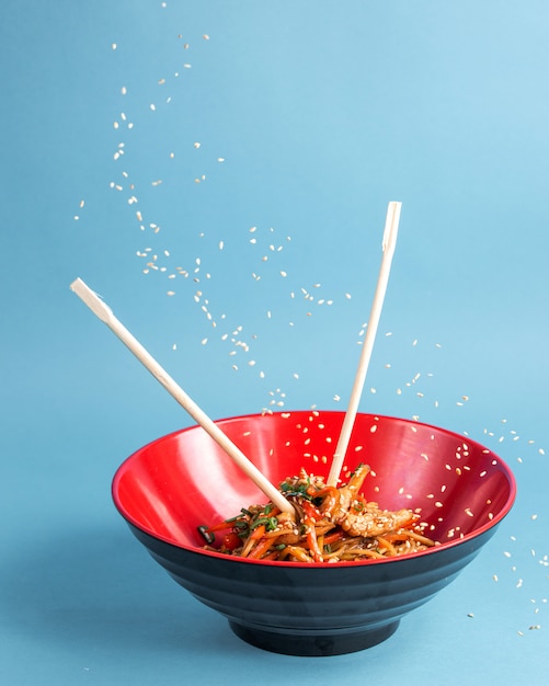 udon sauté de nouilles au poulet, poivron, carotte, sauce soja, oignon de printemps, sésame dans un bol avec des baguettes