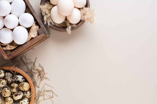 Œufs crus de poulet et de caille placés sur une table beige.