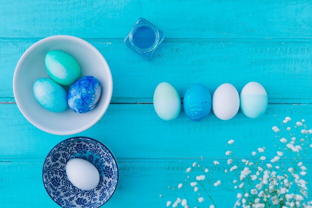 Œufs de Pâques près du pot avec liquide de teinture, assiette et assiette près des fleurs