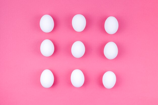 Œufs de poule blancs dispersés sur une table rose