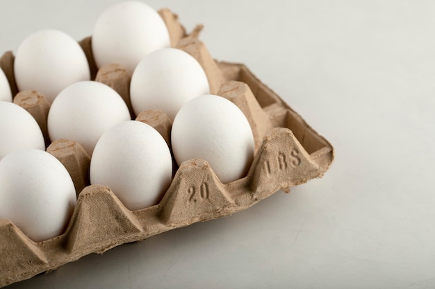 Œufs de poule crus dans une boîte à œufs sur une surface blanche.