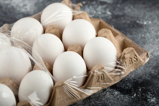 Œufs de poule crus dans une boîte à œufs sur une surface en marbre.