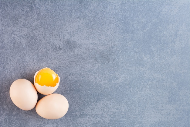 Œufs de poule crus entiers et cassés sur table en pierre.