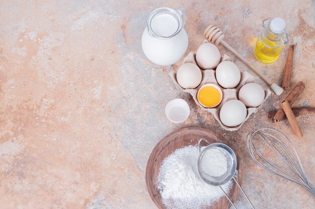 Œufs de poule, lait, farine et épices sur une surface en marbre.