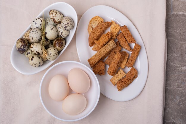 Œufs de poulet et de caille dans une tasse blanche avec des craquelins