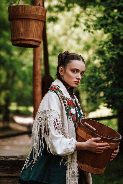 Photo gratuite ukrainienne charmante dans une robe traditionnelle avec un seau dans ses bras