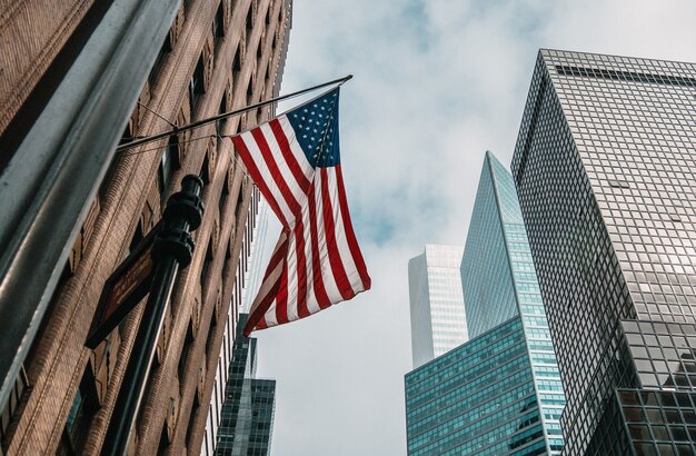 Les USA ou le drapeau des États-Unis d'Amérique sur un mât près de gratte-ciel sous un ciel nuageux