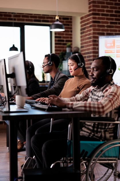 Utilisateur de fauteuil roulant paralysé travaillant à la réception de la ligne d'assistance du centre d'appels avec une déficience physique. Opérateur masculin vivant avec un handicap et des douleurs chroniques, aidant les clients au service client.