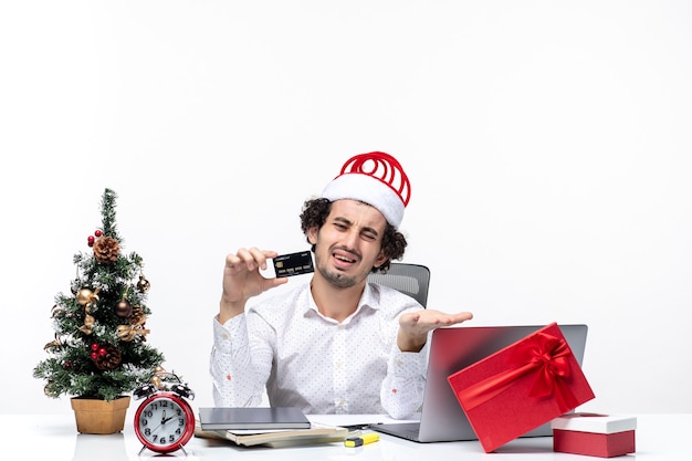 Vacances Ambiance De Fête Avec Jeune Homme Daffaires En Colère Fatigué Avec Chapeau De Père Noël Et Tenant Sa Carte Bancaire Au Bureau Sur Fond Blanc Photo